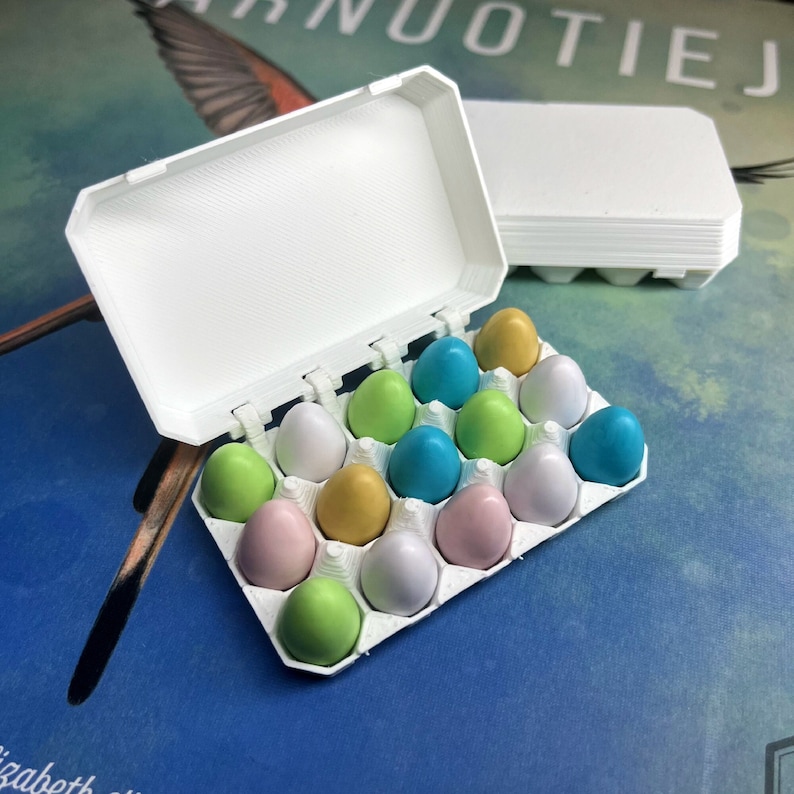 May include: A white plastic egg carton with a hinged lid, filled with colourful pastel-coloured plastic eggs. The eggs are in shades of green, blue, pink, and gold.