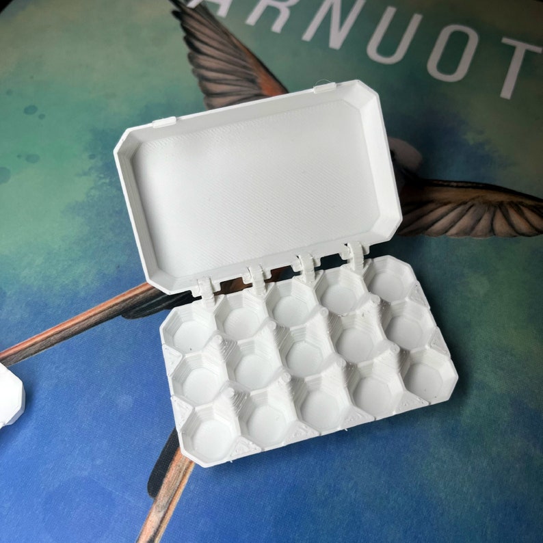 May include: White plastic egg carton with a hinged lid. The carton has 12 individual compartments for holding small items.