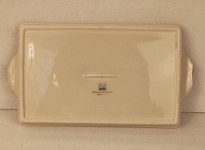May include: Off-white rectangular ceramic serving tray with handles. The tray has a slightly raised edge and a smooth surface. The base of the tray has the text "Blue Sky" and "Microwave and Dishwasher Safe".