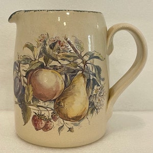 May include: A beige ceramic pitcher with a handle, featuring a hand-painted design of fruit and flowers. The design includes a pear, an apple, strawberries, and plums.