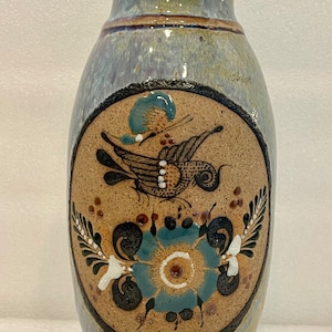 Puede incluir: Un jarrón de cerámica azul y marrón con un diseño pintado de un pájaro y una flor. El jarrón tiene un cuerpo redondeado y una abertura estrecha.