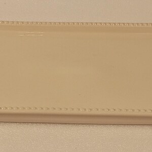 May include: An off-white ceramic serving tray, rectangular in shape, with a beaded edge. It has green holly leaf handles with red berries. The tray is approximately 30 cm long and 20 cm wide, ideal for festive occasions.