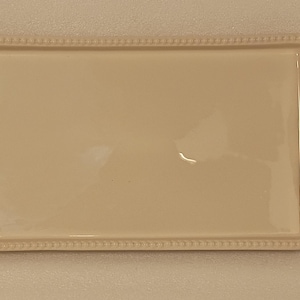 May include: Rectangular off-white ceramic serving tray with a beaded border. The tray features green holly leaf accents with red berries on each end, adding a festive touch. Ideal for serving appetizers or desserts.