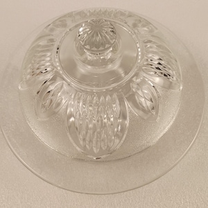 May include: A clear glass cake plate with a matching domed lid. The lid features a decorative floral design and a knob handle. The plate and lid are made of clear glass, allowing the contents to be visible.