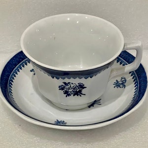 May include: A white teacup and saucer with a blue and white floral pattern. The cup and saucer have a scalloped edge and a blue band around the rim.