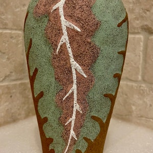 May include: A brown ceramic vase with a green, pink, and white abstract design. The vase has a rounded shape and a narrow opening.