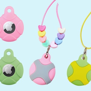 May include: Four round silicone keychains with an Apple logo in the center. Two keychains are pink, one is green, and one is yellow. The pink keychains have a cross pattern on the back. The green keychain has a cross pattern on the back. The yellow keychain has a cross pattern on the back. The keychains are attached to different cords. One cord is yellow, one is pink, and one is a beaded necklace with pastel-colored hearts.