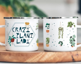May include: Two white enamel mugs with a plant theme. One mug says "Crazy Plant Lady" in a teal hexagon with a green plant illustration. The other mug has a repeating pattern of green plants in pots.