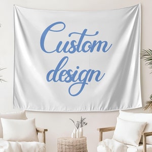 May include: White tapestry with the text "Custom design" in blue cursive lettering. The tapestry is hanging on a white wall in a room with two white chairs and a woven basket.
