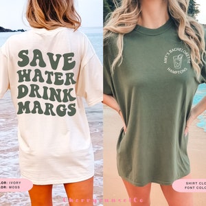 May include: Two women wearing t-shirts. The white t-shirt has the text "SAVE WATER DRINK MARGS" in green. The green t-shirt has the text "AMY'S BACHELORETTE HAMPTONS" in white with a cocktail glass graphic.