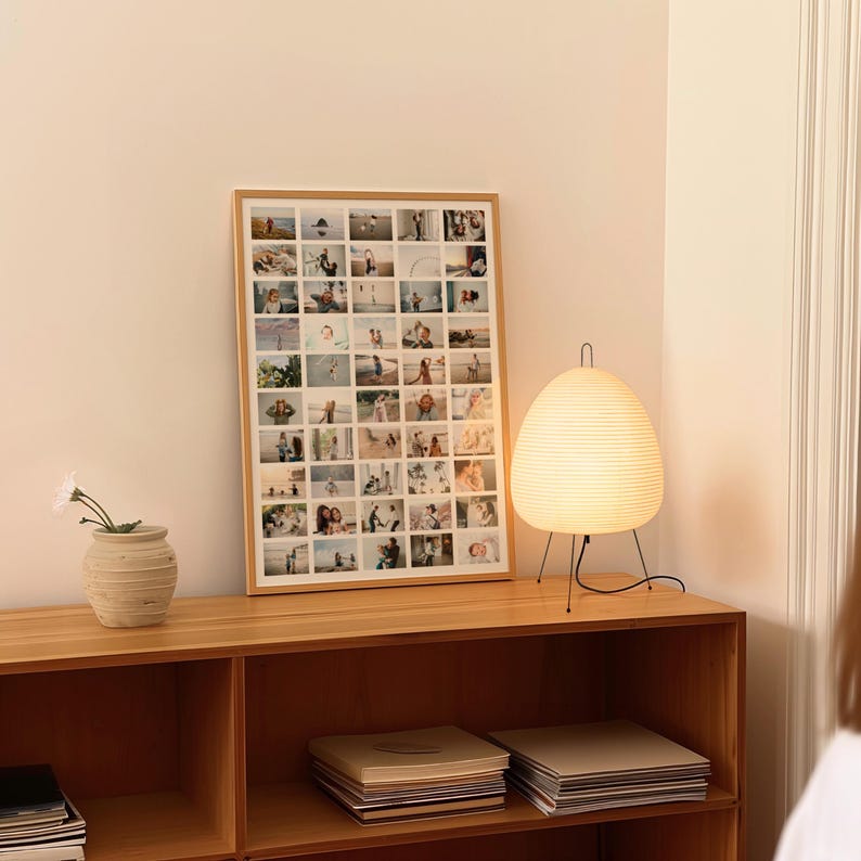 Op de afbeelding: Een ingelijste fotocollage op een houten kast. Een witte papieren lantaarnlamp met zwarte poten staat op de kast. Een kleine vaas met een witte bloem staat ook op de kast.