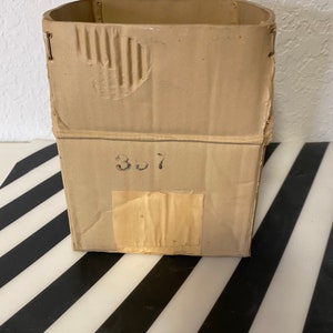May include: A brown cardboard box with the number "307" written on the side. The box is slightly damaged and has a piece of tape on it.