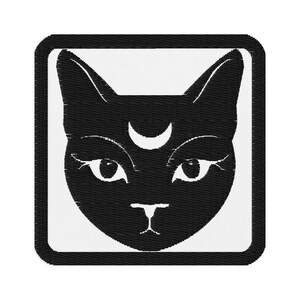 May include: Black cat face patch with a crescent moon on its forehead. The cat's face is in a square frame with a white background. The cat has large eyes and a small nose.