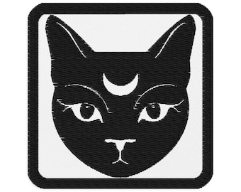 May include: Black cat face patch with a crescent moon on its forehead. The cat's face is in a square frame with a white background. The cat has large eyes and a small nose.
