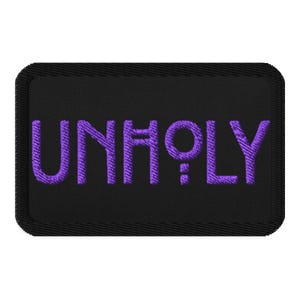 May include: A black embroidered patch with the word "UNHOLY" in purple thread. The patch has a rectangular shape with rounded corners and a stitched border. The text is centered on the patch.