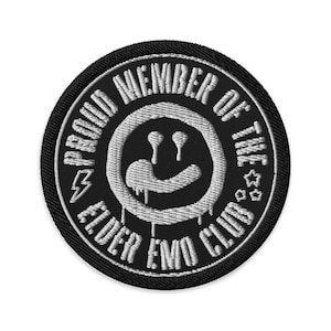 May include: Embroidered black patch with white text and a white smiley face design. The text reads "PROUD MEMBER OF THE EIDER EMO CLUB" around the edge. A lightning bolt and stars are also included in the design.