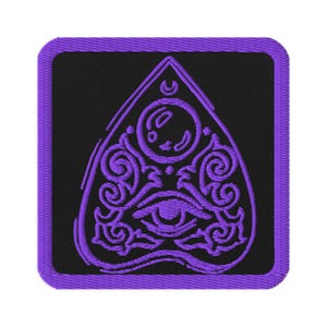 May include: Embroidered patch featuring a purple planchette design on a black background. The planchette has an eye, moon, and ornate swirls. The patch has a purple border and is square with rounded corners.