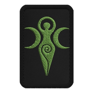 May include: Embroidered patch featuring a green Triple Goddess symbol on a black rectangular background. The symbol depicts a central female figure with arms raised, flanked by two crescent moons. The design has a textured, stitched appearance.