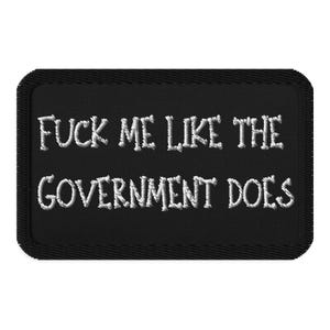 May include: Black rectangular patch with white embroidered text that reads "FUCK ME LIKE THE GOVERNMENT DOES". The patch has a black border and is likely designed to be sewn or ironed onto clothing or accessories.