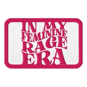 May include: A rectangular patch with a white center and a hot pink border. The patch features the embroidered text "IN MY FEMININE RAGE ERA" in a stylized, wavy font, also in hot pink.