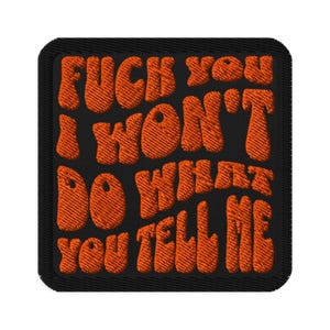 May include: Embroidered patch with the text "FUCK YOU I WON'T DO WHAT YOU TELL ME" in orange, retro-style lettering on a black background. The patch has a black border.