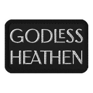 May include: A black rectangular patch with white embroidered text that reads "GODLESS HEATHEN". The patch has a black border and the text is in a bold, sans-serif font.