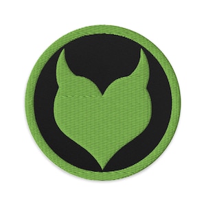 May include: A round, embroidered patch featuring a green stylized heart shape within a black circle, set against a white background. The patch has a green border and a textured appearance, suggesting a fabric material.