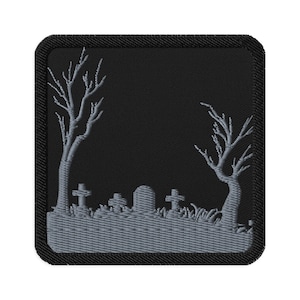May include: Square black patch with a gray embroidered graveyard scene. The design features bare trees, tombstones, and grass. The patch has a black border.
