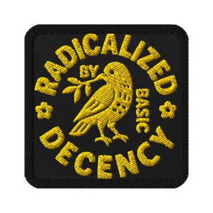 May include: Embroidered patch with the text "RADICALIZED BY BASIC DECENCY" in yellow thread. A yellow bird holding a sprig is in the center. The patch is square with rounded corners and a black background.