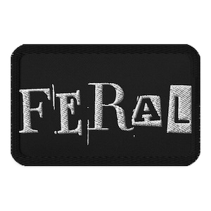 May include: Black rectangular patch with the word "FERAL" embroidered in white. The letters have a distressed, textured appearance, and the patch has a stitched border.
