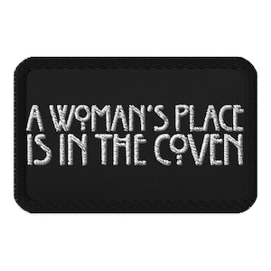 May include: Black embroidered patch with the text "A Woman's Place Is In The Coven" in white. The patch has a rectangular shape with a stitched border. The text includes the female symbol.