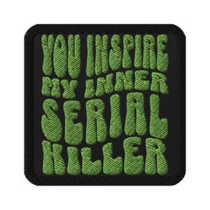 May include: A black square patch with green embroidered text that reads "YOU INSPIRE MY INNER SERIAL KILLER." The text is in a bubble-style font. The patch has a black border.