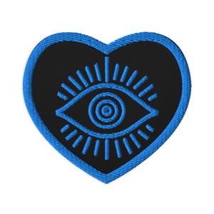May include: A heart-shaped patch with a black center and a blue border. The patch features a blue eye design in the center, with radiating lines. The eye design is surrounded by a blue border.