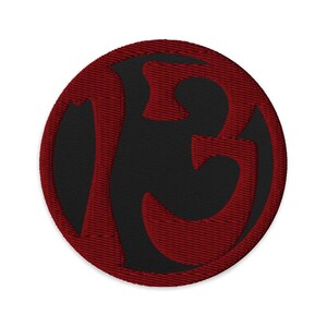 May include: A circular embroidered patch featuring a bold, stylized letter "B" in a deep red color against a black background. The patch has a stitched border, and the design is centered. The patch is likely for clothing or accessories.