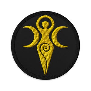 May include: Embroidered patch featuring a gold-colored stylized figure with arms raised, flanked by crescent moons. The figure has a spiral design on the lower body. The patch is circular with a black background and a black border.