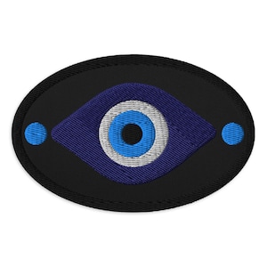 May include: Embroidered patch featuring a blue eye design on a black oval background. The eye has a blue iris, white and blue details, and is flanked by two blue dots. This patch is suitable for clothing or accessories.