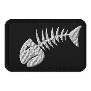 May include: A black embroidered patch featuring a white fish skeleton design. The fish skeleton has a cross for an eye and a sad expression. The patch has a black border.