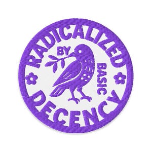 May include: A round, purple embroidered patch with the words "RADICALIZED BY BASIC DECENCY" encircling a purple bird holding a sprig. The bird is centered on a white background.