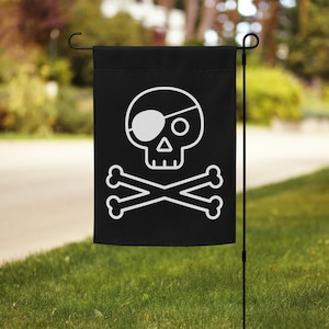 May include: Black garden flag featuring a white pirate skull and crossbones design. The skull has an eye patch and a triangular nose. The flag is displayed on a black metal stand in a grassy yard.