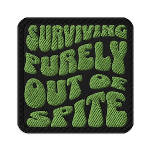 May include: Embroidered patch with the text "SURVIVING PURELY OUT OF SPITE" in green, bubble-style letters on a black background. The patch has a black border and a textured appearance, suggesting a fabric material.