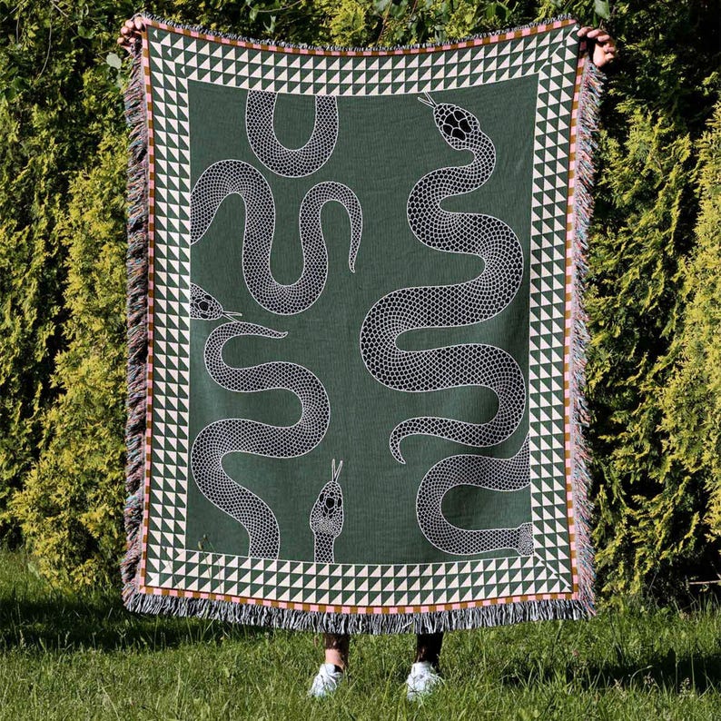 Puede incluir: Una manta tejida verde con un patr&oacute;n de serpiente blanca. La manta tiene un borde de flecos con un patr&oacute;n geom&eacute;trico.