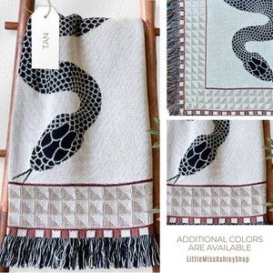 May include: A tan woven throw blanket featuring a black snake design. The blanket has a fringed border and a geometric pattern. The tag on the blanket reads "TAN". Additional colours are available. LittleMissAshleyShop.