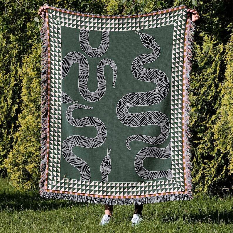 May include: A green woven throw blanket with a white snake pattern. The blanket has a fringe border with a geometric pattern.