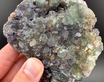 Könnte beinhalten: Ein Cluster aus grünen und violetten Fluoritkristallen mit einer rauen, natürlichen Oberfläche. Die Kristalle sind in einer dichten Formation zusammengefügt und bilden ein visuell interessantes und einzigartiges Stück.