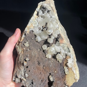 May include: A large, rough, gray rock with a cavity filled with many small, clear quartz crystals.