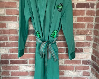 May include: Green hooded robe with a Teenage Mutant Ninja Turtles logo and a striped belt.