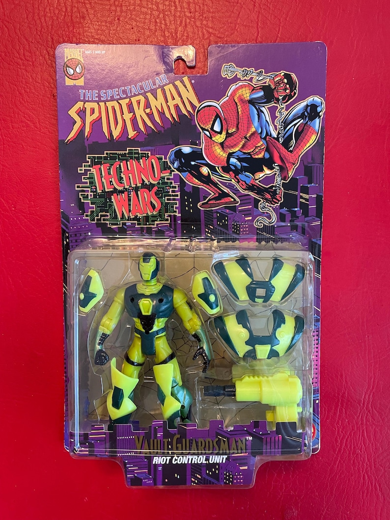May include: A yellow and green action figure of a robot with a gun. The figure is packaged in a plastic blister pack with a cardboard backing. The backing features a cartoon image of Spiderman and the text "The Spectacular Spiderman Techno Wars Vault Guardsman Riot Control Unit".