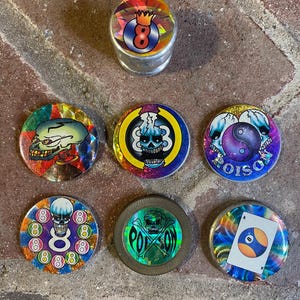 May include: A collection of round, colorful, and metallic novelty items with skull and eight ball designs. One item is a cylindrical grinder with an eight ball graphic. The other items feature various skull and eight ball graphics.