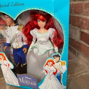 May include: A Special Edition Disney's The Little Mermaid doll set featuring Ariel in a white gown with red hair and Prince Eric. The box is turquoise with gold stars and illustrations of the characters.