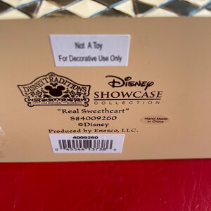 Pu&ograve; includere: Una statuetta in ceramica bianca di Topolino e Minnie Mouse vestiti con i loro iconici abiti rosso e nero. La statuetta fa parte della collezione Disney Traditions Showcase e si intitola "Real Sweetheart". La statuetta &egrave; realizzata a mano in Cina e ha il numero di prodotto 4009260.